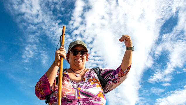 A female hiker giving a thumbs-up during a hike, with a blue sky and white clouds&mdash;altocumulus and cirrocumulus.