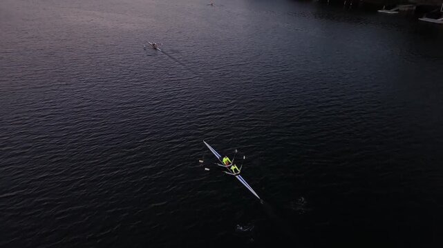 Aerial cinematic footage of women and men rowing across Halifax Harbour at first light, with single and double racing boats moving through the calm coastal waters.