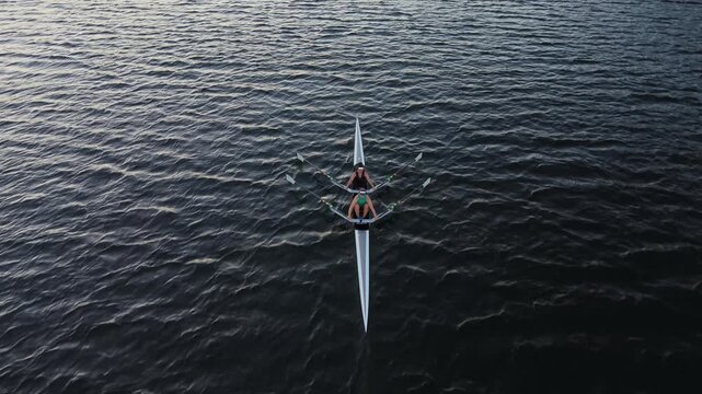 Wide cinematic aerial footage of Halifax Harbour during sunrise, showing male and female athletes practicing competitive rowing in individual and two-person racing boats.