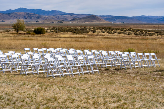 White plastic chairs lined up in rows in a dry meadow for a wedding
