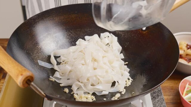 Adding rice noodles to a hot wok/pan with sizzling minced garlic.