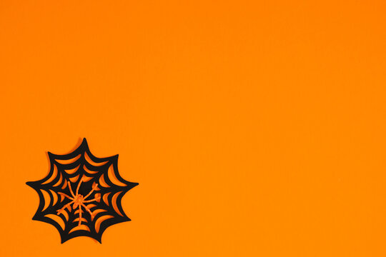 Halloween minimalist background with black decorative spider web on vibrant orange surface. Flat lay modern holiday layout with large copy space for text, advertising, or greeting card template.