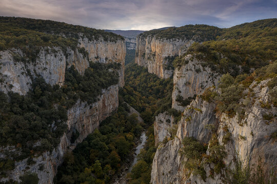 View of Foz de Arbayun canyon with steep limestone cliffs, lush green forest, and a river flowing through the gorge in Usun, Navarra, Spain.