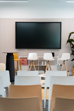 View of a modern presentation space featuring a large screen, white stools, and rows of chairs in London, United Kingdom.