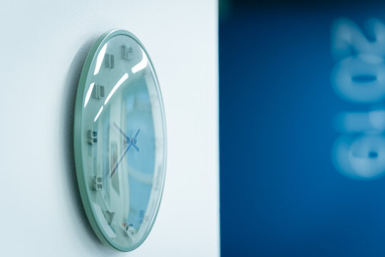 View of a modern wall clock with a light green frame mounted on a white wall in London, United Kingdom.