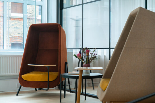 View of modern high-backed armchairs with yellow cushions and a small table with a flower vase in a contemporary office space in London, United Kingdom.