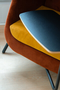 View of a modern Office Mix chair with a vibrant yellow cushion, rust-colored velvet frame, and black integrated desk surface on a light wooden floor in London, United Kingdom.