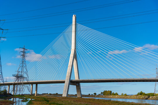 View of the Flintshire Bridge, a cable-stayed bridge with a tall concrete pylon and steel cables, crossing the River Dee with electricity pylons in Deeside, Wales, United Kingdom.