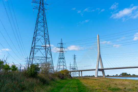 View of the Flintshire Bridge with tall electricity pylons and power lines stretching across the landscape under a clear blue sky in Deeside, Wales, United Kingdom.