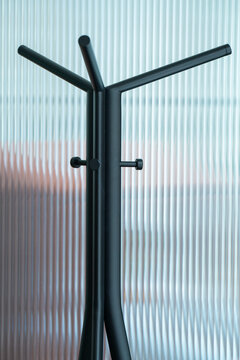 View of a modern black metal coat rack with multiple hooks standing against a textured, translucent fluted glass wall in London, United Kingdom.