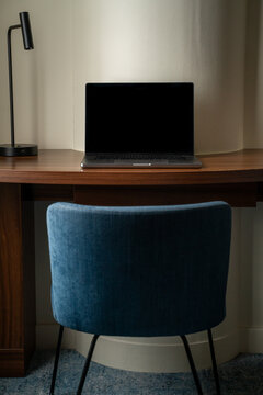View of a laptop on a wooden desk with a blue chair and a desk lamp in London, United Kingdom.