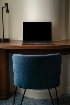 View of a laptop on a wooden desk with a modern lamp and a blue chair in a workspace in London, United Kingdom.