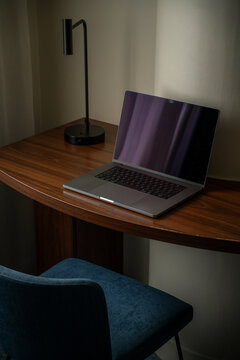 View of a laptop on a wooden desk with a modern lamp and a blue chair in an office setting in London, United Kingdom.