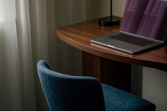View of a laptop on a wooden desk with a blue upholstered chair in a modern office setting in London, United Kingdom.