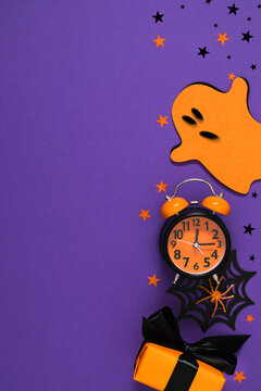 Halloween background with orange alarm clock, cute ghost, gift box, spider web, and stars on purple background. Vertical flat lay festive creative countdown layout with empty copy space.