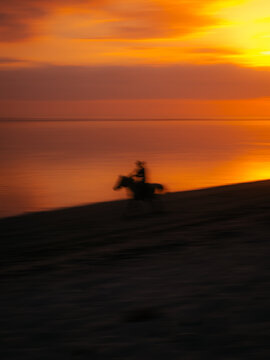 View of a silhouette of a person riding a horse on the beach during a vibrant sunset at ARYA Sumba - Kodi, Kodi, East Nusa Tenggara, Indonesia.