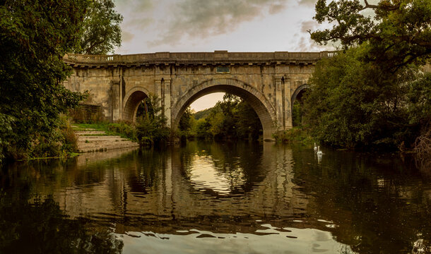 Swans swim under the historic Dundas Aqueduct bridge at sunset.