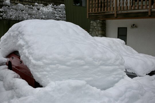 View of cars completely buried under a thick layer of fresh snow parked in front of a building in Whistler, British Columbia, Canada.