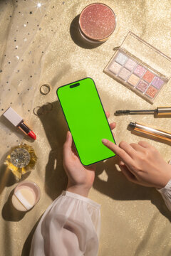 Woman's hands holding blank screen smartphone amongst makeup items