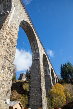 View of the historic stone Ravenna Viaduct arch bridge spanning a valley in the Black Forest, surrounded by autumn trees under a clear blue sky in Freiburg, Baden-Wurttemberg, Germany.