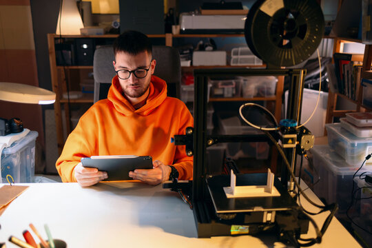 Man Using Tablet Next to 3D Printer in Home Workshop