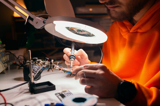 Young Technician Soldering Electronics Under Magnifying Lamp