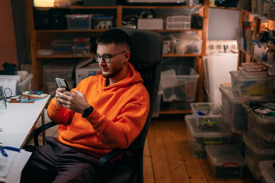 Young Man in Electronics Workshop Checking Smartphone