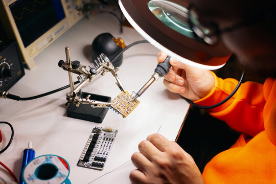 Engineer Soldering Circuit Board Under Magnifying Lamp
