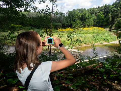 Child photographing a meadow and stream with a digital camera