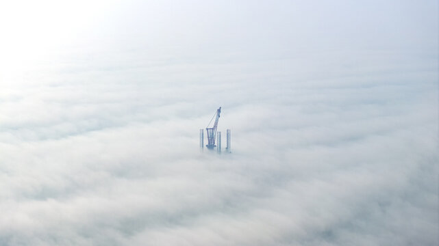Offshore wind installation crane above sea of clouds in heavy sea fog
