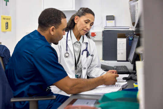 Two medical professionals in hospital scrubs talk at a desk