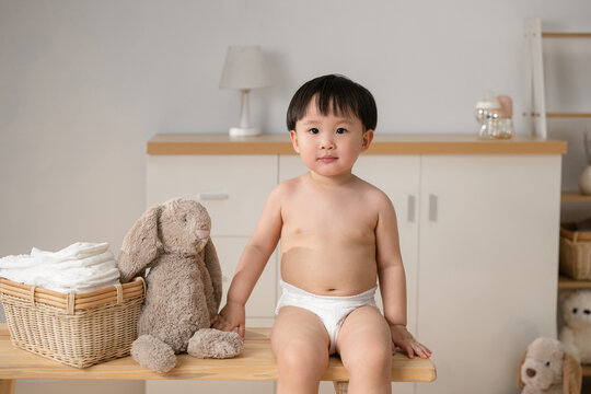 Cute Toddler in Diaper sits on a wooden bench next to a stuffed bunny