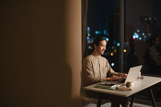 Man Working on Laptop at Desk in City Apartment at Night