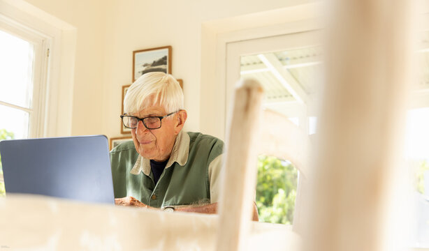 elderly man (90) looking at laptop in light filled room