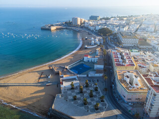 High-angle morning view of La Caleta beach and the city promenade, featuring buildings with colorful roofs and tranquil Atlantic Ocean waters dotted with small white boats. Cadiz, Andalusia, Spain. © nzatravel