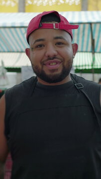 Close-up portrait of smiling young Brazilian vendor in red backwards cap at street market