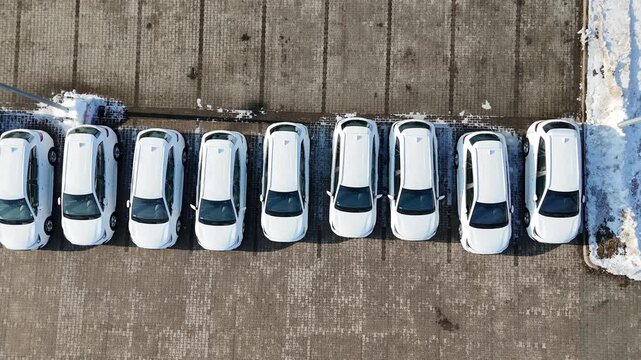 Aerial view of multiple new white cars parked in a straight line on a snow-covered parking lot at a car dealership, commercial auto showroom display, brand new vehicles for sale, modern automotive ret