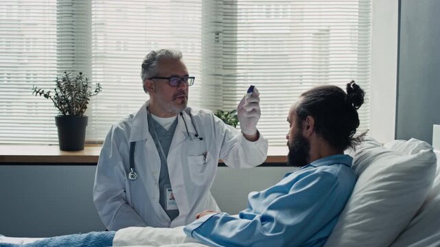 Middle aged Caucasian doctor measuring temperature of hospitalized patient with digital infrared thermometer and writing notes. Suitable for medical care commercials and healthcare advertising