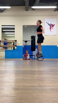 Woman exercising in rebound boots as child watches in fitness studio. Kangoo jumps workout and family fitness. Rebounding cardio exercise. Indoor training class.