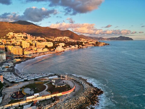 Sturla beach and the coast of Genoa towards Quarto, Nervi and the Portofino promontory in warm sunset light, with a seaside park and breakwater, aerial view, Italy