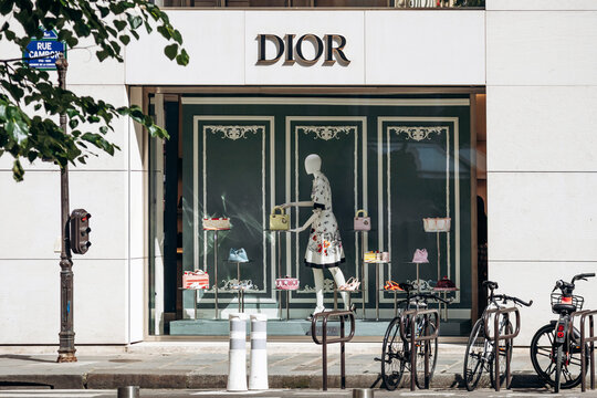 Paris, France - May 23, 2026: Dior boutique window display on Rue Cambon featuring a mannequin in a floral dress, designer handbags, shoes and accessories, with bicycles parked outside.