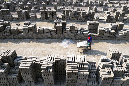 Aerial view of a brickyard with rows of stacked clay bricks and a worker pushing a cart in Gaibandha Sadar Upazila, Rangpur Division, Bangladesh.