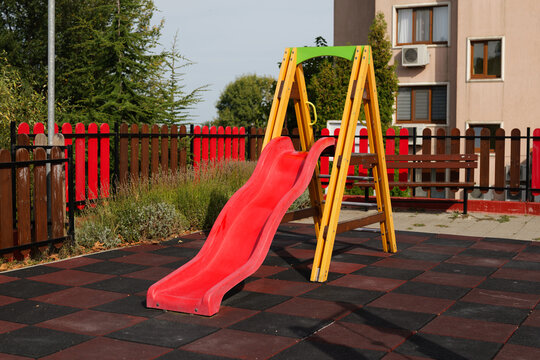 Colorful wooden children slide with a bright red chute on a playground near a building.