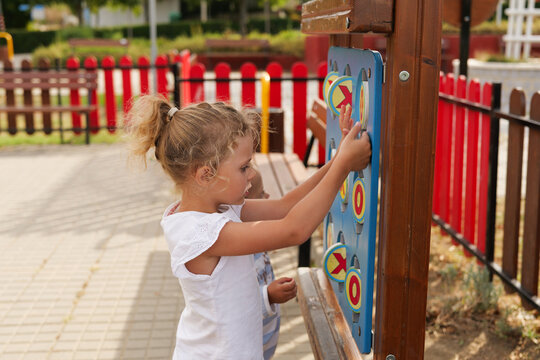 Little curly girl playing tic-tac-toe game panel on an outdoor playground in summer.