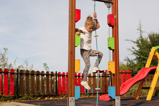 Little girl climbing up a rope on a colorful playground climbing structure on a sunny day.