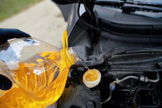 Person pouring yellow antifreeze liquid from bottle into car's washer fluid reservoir. Gloved hand tilting large bottle to pour yellow screen wash into car windscreen water tank. Selective focus