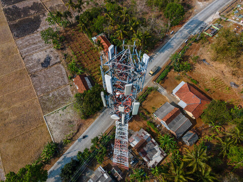Aerial view of Karangrena telecommunications tower surrounded by rural houses, palm trees, and agricultural fields in Central Java, Indonesia.