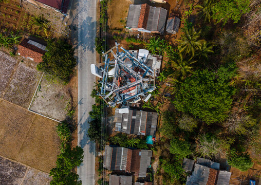 Aerial view of a telecommunications tower situated among rural houses, lush palm trees, and agricultural fields in Central Java, Indonesia.