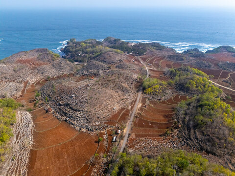 Aerial view of terraced fields and rocky hills along the coastline with a road winding through the landscape in Gunungkidul Regency, Special Region of Yogyakarta, Indonesia.