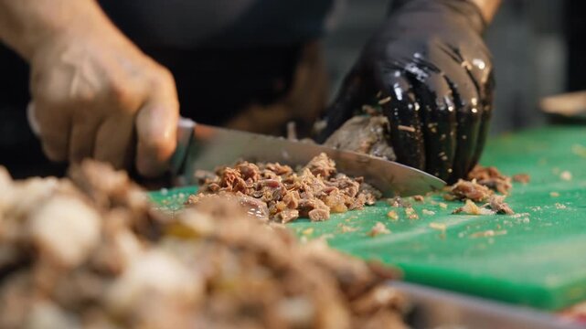 Chef chops cooked meat for serving with Uzbek wedding plov on a green cutting board. Banquet catering, food preparation, traditional cuisine, professional kitchen, Central Asian culture